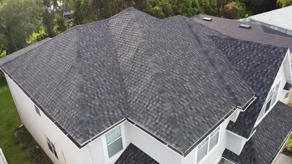 Aerial view of a completed residential hip roof with dark gray architectural shingles